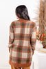 A woman viewed from behind wearing a long-sleeve knit cardigan with a large plaid pattern in rust orange, beige, and dark brown.