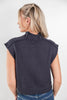 A woman shown from the back wearing a dark charcoal ribbed knit sleeveless top with shoulder detailing, paired with blue jeans, against a plain light gray background.
