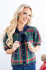 A woman wearing a short-sleeve knit cardigan with a navy, green, and red plaid pattern and a knotted tie neckline, paired with blue jeans.