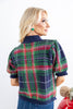 A woman from behind wearing a short-sleeve knit cardigan with a navy, green, and red plaid pattern.