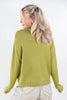 A woman with blonde hair, viewed from behind, wearing a textured olive green knit sweater and striped pants against a plain white background.