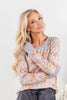 A woman wearing a gray long-sleeve crewneck sweatshirt with a pastel floral pattern in pink, orange, and yellow.