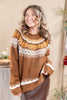 A woman wearing a brown knit sweater with white and orange Fair Isle patterns, featuring pumpkin motifs across the chest, posing in a warm indoor setting.