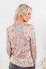 A woman shown from the back wearing a long-sleeve gray top with a dense pastel floral print in pink, peach, orange, and cream.