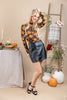 A woman models a long-sleeve black mesh top with an orange and yellow floral pattern, paired with a black faux-leather mini skirt and black strappy heels, in a styled indoor autumn setting with pumpkins, a table, and a ladder.