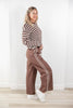 A woman modeling a brown and white striped long-sleeve top with matching brown wide-leg pants featuring white side stripes, paired with white sneakers, standing against a white wall.