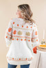 A woman shown from the back wearing a cream knit sweater with orange and tan autumn-themed patterns, including acorns, pumpkins, and turkeys, paired with blue jeans.