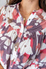 Close-up of a woman wearing a sheer floral blouse with a ruffled collar and button front. The fabric has a large-scale abstract floral print in white, dusty pink, and muted purple.