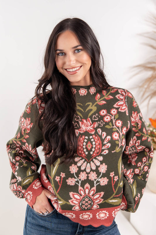 A woman wearing a long-sleeve mock neck sweater with a green base and a red, pink, and white floral pattern.