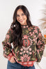 A woman wearing a long-sleeve mock neck sweater with a green base and a red, pink, and white floral pattern.
