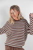 A woman wearing a brown and off-white horizontally striped knit sweater, shown from the waist up against a plain light gray studio background.