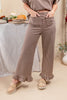 A woman wearing brown and beige gingham wide-leg pants with ruffled hems, paired with a matching gingham top and beige loafers, standing in a softly styled indoor setting.