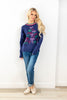 A woman modeling a navy blue crewneck sweater with colorful embroidered bows, paired.