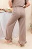 A woman shown from the back wearing brown and beige gingham wide-leg pants with ruffled hems, paired with beige slip-on shoes in a softly lit indoor setting.