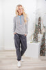 A woman modeling a long-sleeve striped henley shirt with a light blue placket, paired with dark gray drawstring pants and white sneakers.