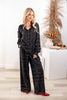 A woman models a black long-sleeve button-front shirt and matching wide-leg pants set with a white geometric line pattern, styled with red pointed-toe heels.
