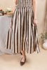 A woman wearing a brown and cream vertical striped midi dress with a smocked bodice and pleated skirt, paired with dark brown pointed flats. 