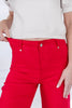 Bright red high-waisted jeans worn by a woman, shown from the waist down with hands pulling the fabric outward to demonstrate the stretch.