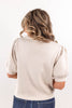 A woman viewed from behind wearing a light beige short-sleeve top with puffed sleeves and blue jeans, set against a plain white background.