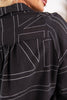 Close-up of a black blouse with white geometric dashed stitching, showing the back of the garment and part of a woman's neck and lower face.