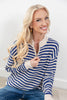 A smiling blonde woman wearing a blue and cream striped knit half-zip sweater and blue jeans, posed against a clean white wall.