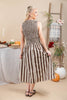 A woman modeling a sleeveless midi dress with vertical brown and cream stripes, shown from the back in a warm, autumn-themed room decorated with pumpkins, a table, and a ladder.