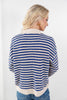 A woman shown from the back wearing a blue and cream striped knit cardigan sweater with blue jeans, set against a plain white studio background.