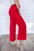 A woman wearing bright red wide-leg cropped pants with a light beige top and beige heeled sandals.
