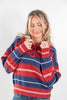 A woman wearing a red, navy, and white striped knit sweater with a buttoned collar, paired with blue jeans, against a plain light gray background.