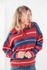 A woman wearing a red, navy blue, and white striped knit polo sweater with blue jeans, standing against a plain white background.