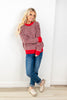 A woman wearing a red, white, and black patterned knit sweater, blue jeans, and beige loafers.