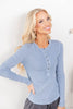 A woman wearing a light dusty blue long-sleeve henley shirt with a button placket.