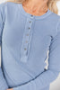A close-up of a woman wearing a light blue ribbed long-sleeve henley top with a button placket.