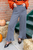 A person wearing black and white gingham wide-leg pants with ruffled hems, paired with an orange sweatshirt and black pointed flats, standing outdoors near hay bales, pumpkins, and green steps.