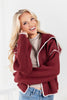 A woman wearing a chunky ribbed knit cardigan in deep burgundy with white contrast trim.