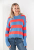 A woman wearing a blue and coral red striped knit sweater with blue jeans, standing against a plain white wall.