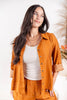 A woman wearing a matching burnt orange linen two-piece set with white line-art patterns, featuring a long-sleeve button-up shirt and coordinating pants, styled over a white ribbed tank top.