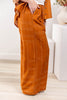 A woman wearing wide-leg orange trousers with a white geometric line pattern, paired with a white top and a matching orange top.