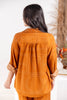 A woman viewed from behind wearing a loose orange-brown top with white geometric line patterns and rolled sleeves, paired with matching bottoms.
