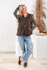 A woman models a brown patterned button-up vest over an olive green long-sleeve shirt, paired with distressed light blue jeans and brown loafer shoes.