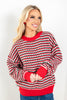 A woman wearing a festive red, green, and white striped knit sweater with blue jeans.