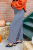 A person wearing black and white gingham wide-leg ruffled pants and black pointed flats with gold hardware, standing outdoors next to a brick wall, hay bales, pumpkins, and green stairs.