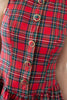 Close-up of a red tartan plaid garment with green, yellow, and white stripes, featuring a front button closure with gold-tone circular rings.