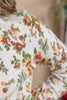 Close-up of a person wearing a cream-colored knit top with a vintage floral pattern in orange, green, and yellow.