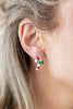 A close-up of a woman's ear wearing a small silver stud earring with a dangling candy cane charm in red, white, and green enamel.