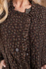 A close up of a brown ruffled button-front vest with a small floral pattern over a dark olive green long-sleeve shirt.