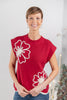 A woman wearing a red ribbed knit sweater top with large white floral patterns on the front.