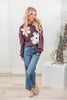 A woman wearing a mauve crewneck sweatshirt with large white flower appliques.