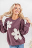 A woman wearing a mauve crewneck sweatshirt with large white flower appliques, paired with blue jeans.