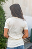 The back of a woman wearing a cream colored short sleeve t-shirt.